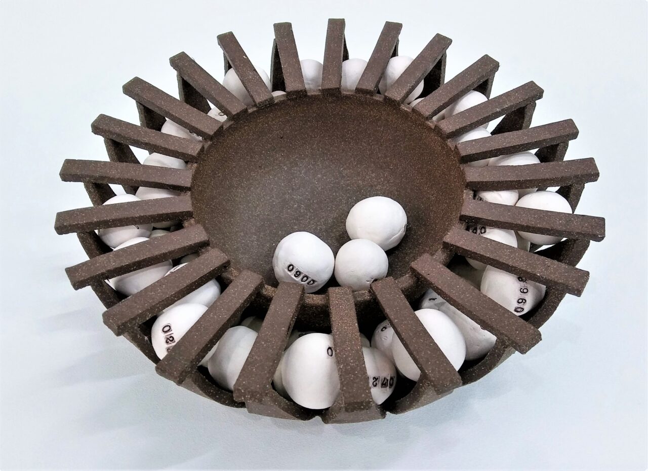 Ceramic sculpture of a round bowl surrounded by bars containing round pieces marked with numbers